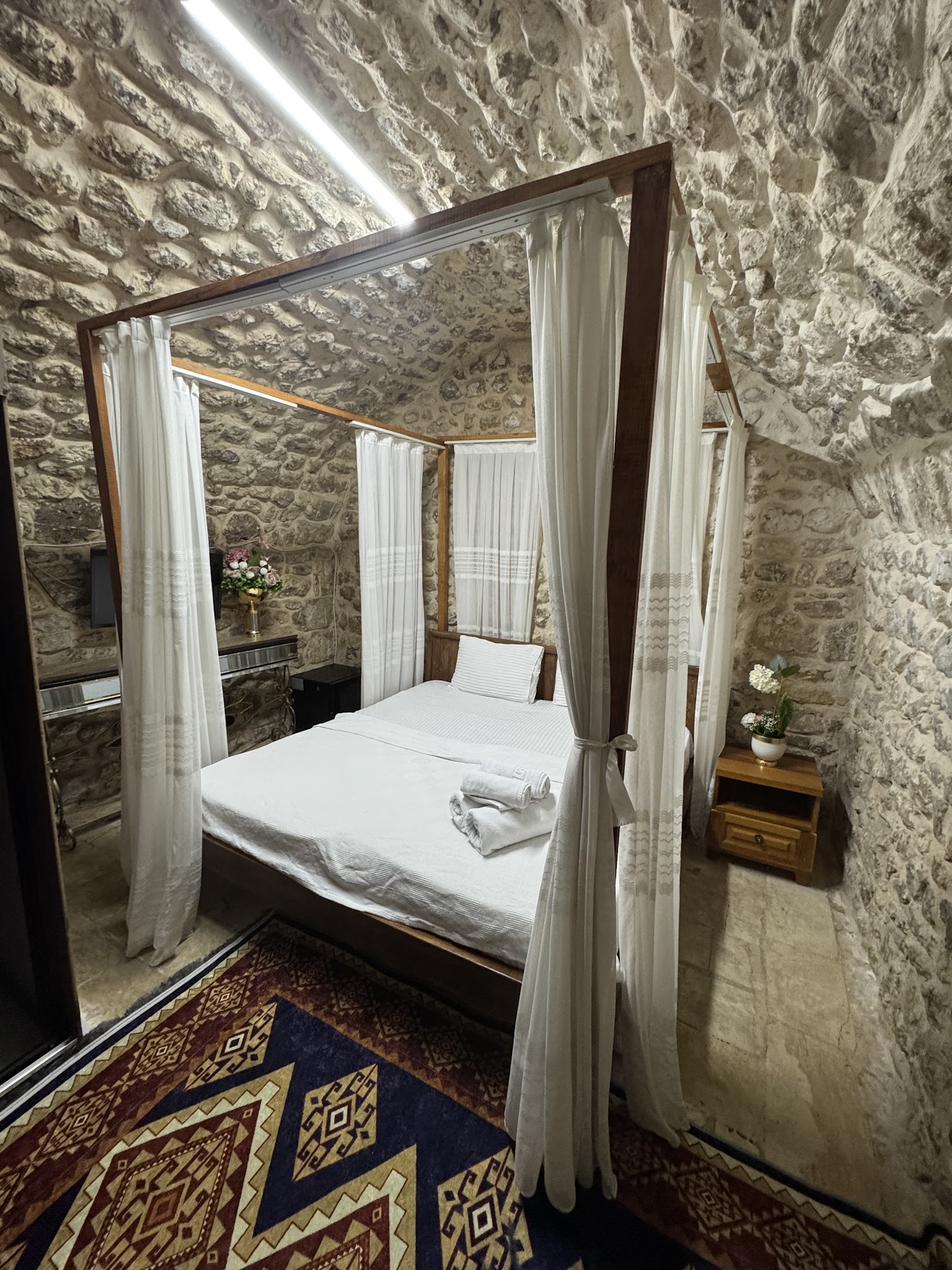 Taş duvar önünde beyaz tül ve otel yatağı